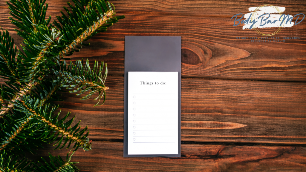 Holiday to-do list on a wooden table with pine branches and the Body Bar MD logo in the corner.