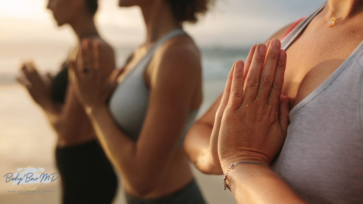 Group of women practicing mindfulness with hands in prayer position during a wellness session at Body Bar MD.