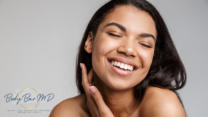 Smiling woman with glowing skin, touching her face in a joyful expression, showcasing confidence and wellness.