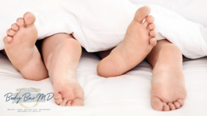 Close-up of two pairs of feet under a white blanket, symbolizing intimacy and relaxation.