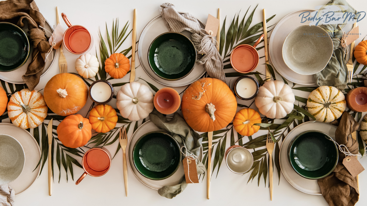 Thanksgiving table setting with pumpkins, greenery, candles, and earthy-toned tableware.