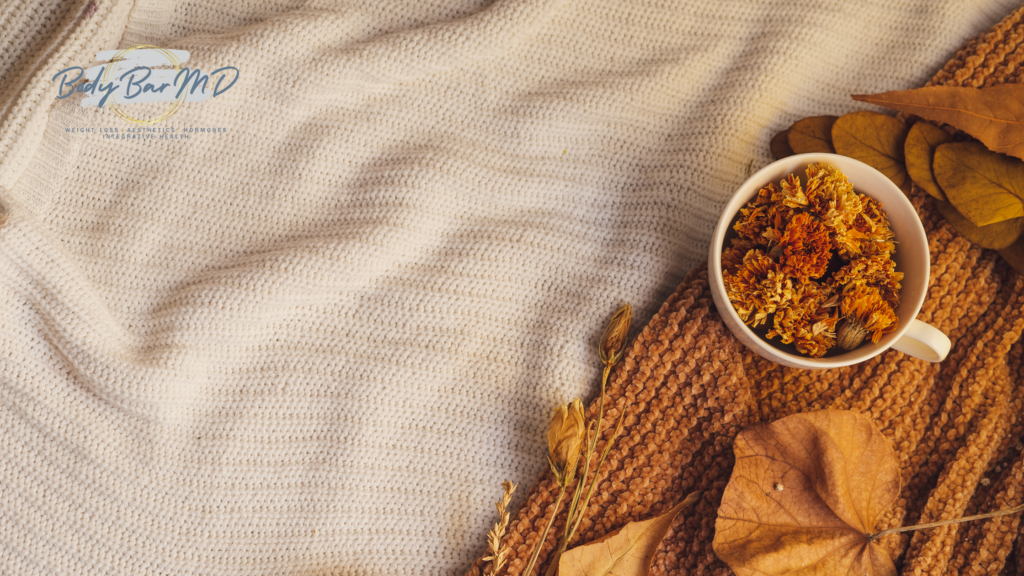 Cozy fall setting with dried flowers in a mug on a knitted blanket surrounded by autumn leaves.