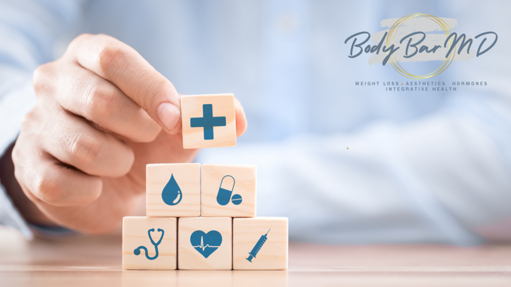 Hand placing a wooden block with a medical cross on a stack of health symbols, symbolizing holistic health and wellness with Body Bar MD’s logo in the background.