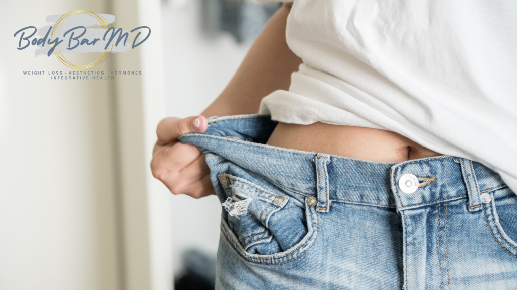 Person wearing loose jeans, showing weight loss progress, with the Body Bar MD logo visible. The image symbolizes successful weight management and body transformation.