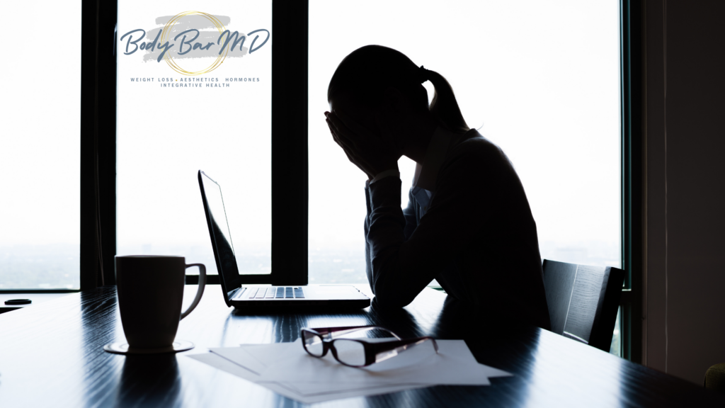 Silhouette of a stressed person sitting at a desk with a laptop, head in hands, with the Body Bar MD logo in the corner. This image represents stress and burnout.