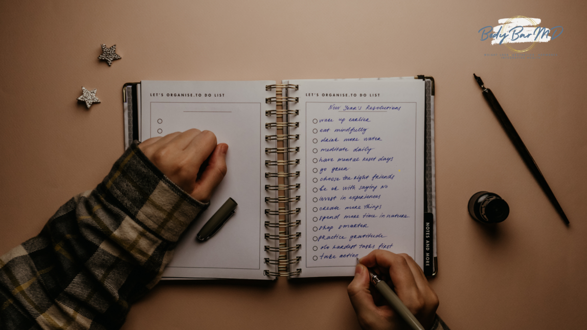 A person writing New Year’s resolutions in a planner, surrounded by a pen, ink, and decorative stars.