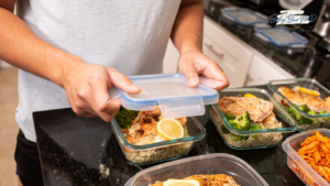 Person preparing healthy meal prep containers with salmon, broccoli, and rice in a kitchen.