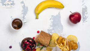 A mix of healthy and unhealthy foods, including a banana, apple, sandwich, fries, and coffee on a textured surface.