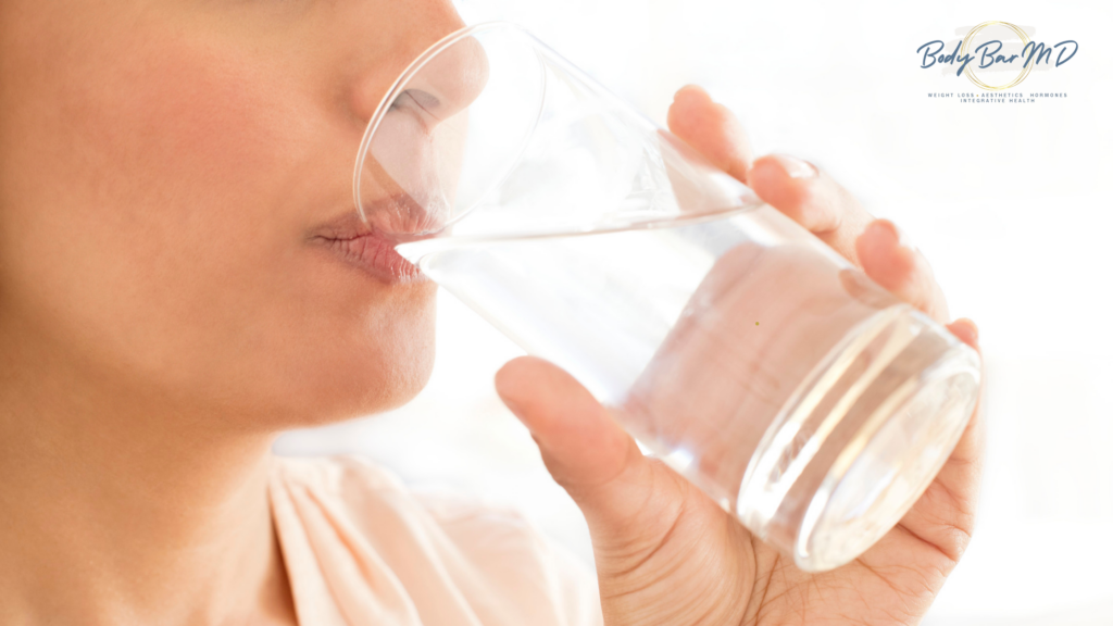 A close-up of a woman drinking a glass of water, highlighting the importance of hydration.