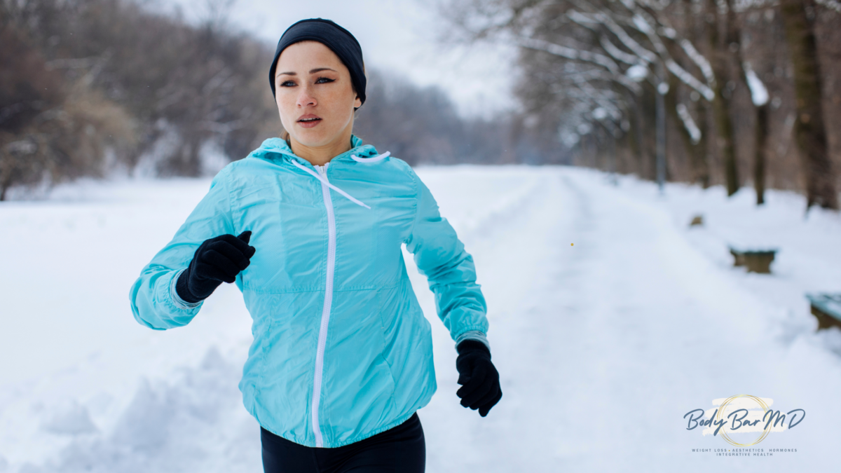 A woman jogging outdoors in the snow, wearing a blue jacket and black gloves, staying active during winter.