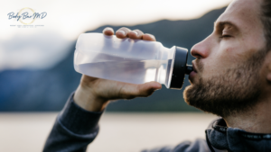 A man drinking water from a reusable bottle outdoors, emphasizing the importance of staying hydrated for health.