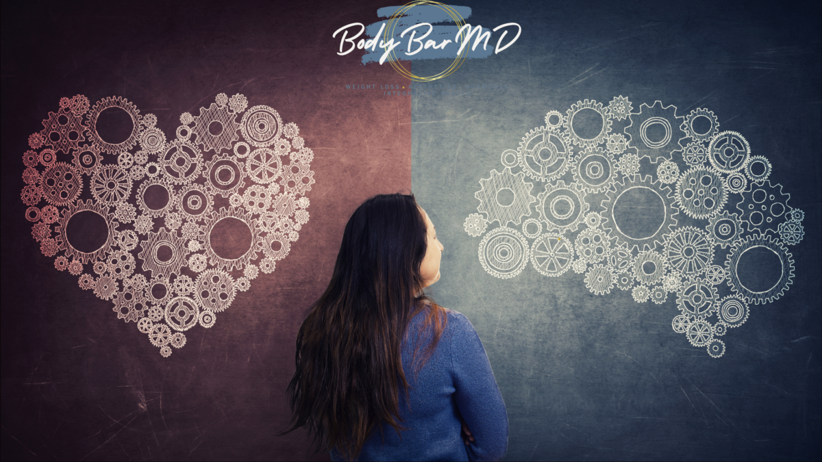 A woman stands thoughtfully between a heart made of gears on the left and a brain made of gears on the right, symbolizing the connection between emotional and mental health. The Body Bar MD logo is displayed at the top.