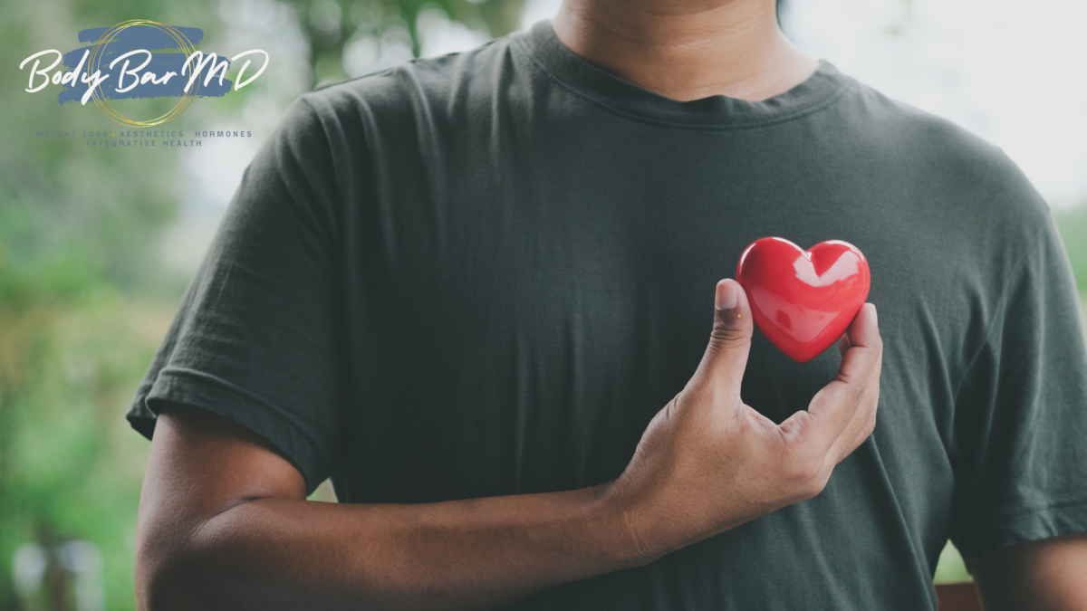 A person in a dark green shirt holding a red heart, symbolizing heart health and self-care.