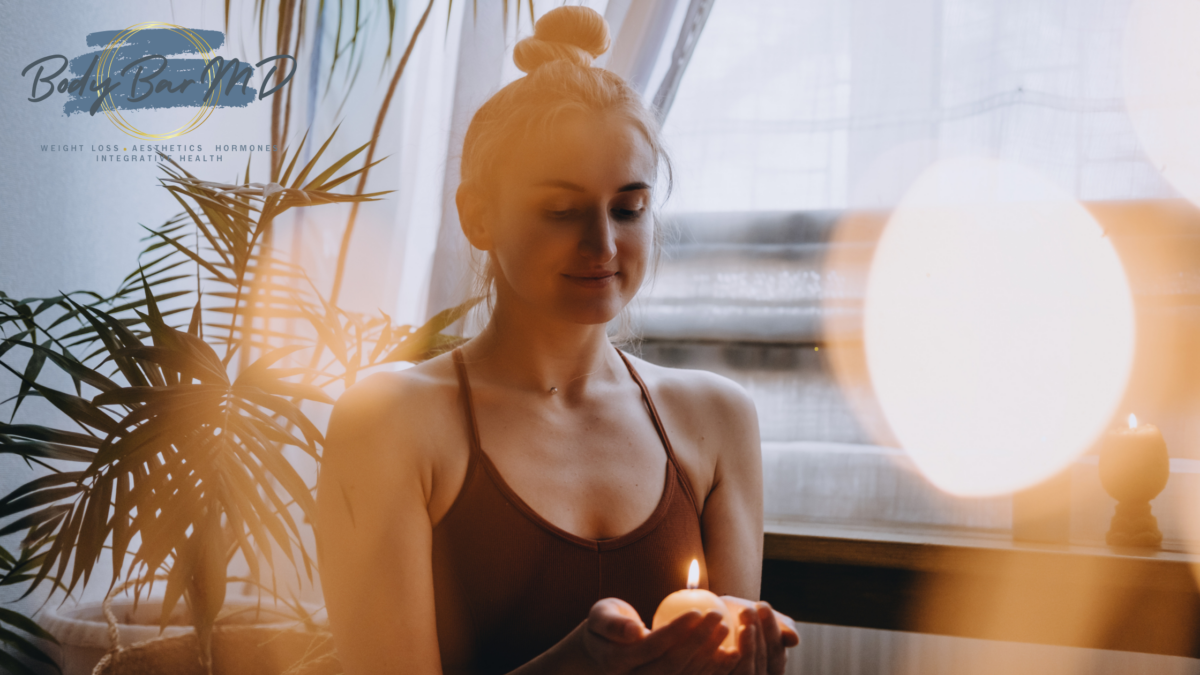 A serene woman holding a lit candle, surrounded by plants, embracing mindfulness and self-care in a peaceful environment.